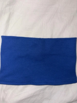 Blå stickad tubhalsduk - Säljer en enkel blå tubhalsduk i. Buffen är helt slät utan mönster eller detaljer och har en klassisk, rak form. Perfekt att styla över en skjorta eller t-shirt för en clean look. Eller skidåkning/sport.