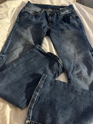 Blå raka jeans med klassisk passform - Säljer ett par blå jeans med rak passform och klassisk femficksdesign. Jeansen har normal midja, Snygga kontrastsömmar och tidlös look som funkar till det mesta. Perfekta för dig som gillar enkel och stilren stil.