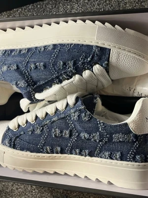 Blå numeris sneakers med vit sula - Säljer ett par unika sneakers i blå denim med slitna detaljer och vit, räfflad sula. Skorna har vita snören och vita detaljer vid häl och plös. Perfekta för dig som vill sticka ut med en cool streetstyle-look. Köpte ifrån numeris storlek 42.