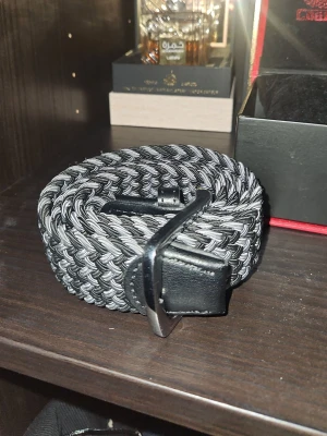 Gråsvart flätad bälte - Helt nytt skärp inga som hälst täcken på användning, köpt för cirka [220kr]Säljer ett snyggt flätat bälte i svart och grått med metallspänne och detaljer i svart konstläder. Perfekt accessoar för att lyfta din outfit med en modern touch. Passar till både jeans och chinos.