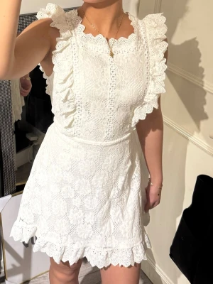 Vit studentklänning/spetsklänning med volang - Supersöt vit spetsklänning med volangdetaljer längs axlar och nederkant. Klänningen är ärmlös, har rund halsringning och ett knytband i midjan för extra form. Perfekt för sommarens alla tillfällen. Använd en gång🤍passar både Xs o S. Men är storlek S