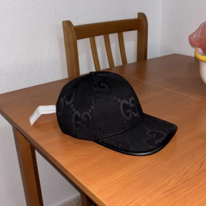 Svart keps från Gucci med GG-mönster - Snygg svart keps från Gucci med klassiskt GG-mönster ton-i-ton över hela kepsen. Kepsen har böjd skärm med svart kant i läderlook och justerbart spänne bak. Perfekt för dig som vill sticka ut med en lyxigare stil. Hör av dig vid minsta fundering!👍🏼 (pris är ej hugget i sten)🔥🔥🔥