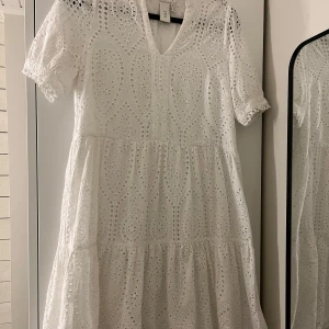 Vit kortklänning från YAS i broderad bomull - Superfin vit kortklänning från YAS i broderad bomull med v-ringning och korta ärmar. Klänningen har ett detaljerat hålmönster och volang i kjolen, vilket ger en romantisk och luftig känsla. Endast använd en gång så den är som ny!🤗