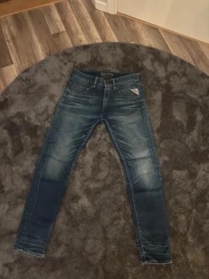 Replay blå jeans  - Säljer ett par blå Replay jeans med slim passform. Jeansen har snygga slitningar och tvättade detaljer, samt Replay-logga på fickan och bak vid linningen. Tillverkade i slitstarkt jeansmaterial med smal siluett.