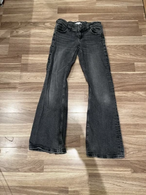 Svarta bootcut jeans Gina Tricot - Säljer ett par svarta bootcut jeans från Gina Tricot i storlek 146. Jeansen har klassisk femficksdesign, dubbla knappar i midjan och lätt utsvängda ben. Materialet är jeans med en tvättad look och rå kant längst ner på benen för en extra cool vibe.