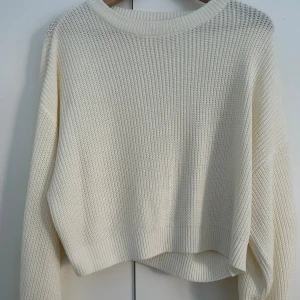 Vit stickad tröja - Säljer en vit stickad tröja med grov struktur och rund hals. Tröjan har långa ärmar och breda ribbade muddar vid ärmslut och nederkant. Perfekt för lager på lager under kyliga dagar.