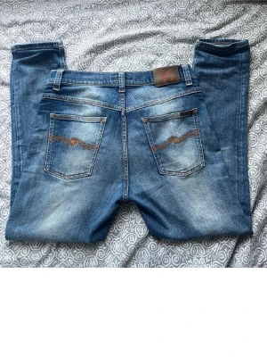 Blå jeans från Nudie Jeans riktigt feta shades 30 W 31 L - Har andvänt länge. Storlek 28 W 29 L  men sitter som 30 W 31 L. Säljer ett par klassiska blå jeans från Nudie  Jeans med snygg slitning och kontrastsömmar. Modellen har raka ben, fem fickor och en cool detalj med vågigt mönster på bakfickorna. Tillverkade i mjukt bomullsmaterial för skön passform.