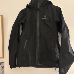 Arc'teryx beta AR jacka, dam storlek S - Köpt ny på naturkompaniet.  Använd fåtal gånger.  Dragkedjor i armhålorna. Går att dra åt både i midjan och på luvan.  Kardborret vid ärmarna funkar som det ska. Alla dragkedjor funkar. Impregneringen funkar som den ska. Smått missfärgad vid kragen pga smink. Jag har skrubbat lite snabbt med vatten och lite diskmedel så det borde inte vara några problem att få det helt fläckfritt. Nypris på naturkompaniets hemsida: 6499kr