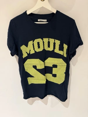 Mörkblå t-shirt från Mouli med tryck - Cool mörkblå t-shirt från Mouli med stort gult mesh-inspirerat tryck framtill och två gula ränder på ryggen. Klassisk rund hals och korta ärmar. Perfekt för dig som gillar sportig streetstyle och vill sticka ut med en unik design.