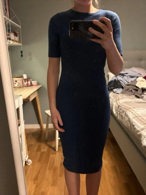 Marinblå tight klänning - Säljer en marinblå, tight klänning med korta ärmar och rund hals. Klänningen är midilång och har en enkel, stilren design som sitter snyggt mot kroppen. Perfekt för dig som gillar minimalistisk stil.