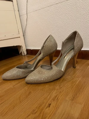 Glittriga pumps från Tamaris, strl 40 - Glittriga silver/champange färgade tamari’s klackskor med blank klack i stl 40. Jätte fina till fest/bal eller bara till vardags! Väldigt bekväma och lagom höga. Säljer pågrund av för stor storlek, brukar själv ha stl 39. Jag har köpt dem på Sellpy och därav finns det tydliga spår av användning på sulan under skon, samt små märken på själva klacken.