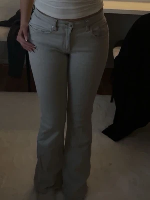 Ljusgrå bootcut jeans - Säljer ett par ljusgrå jeans med bootcut passform och klassisk femficksdesign. Byxorna har låg midja och är tillverkade i ett mjukt bomullsmaterial med lite stretch. 