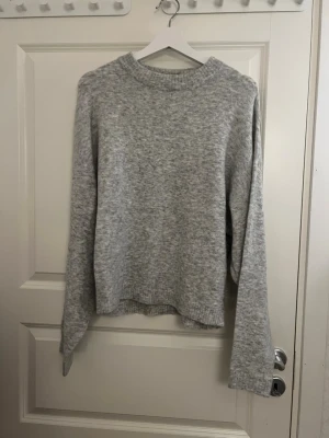 Grå stickad tröja från Nelly - Mysig grå stickad tröja från Nelly i storlek S. Tröjan har en enkel och clean look med rund halsringning, långa ärmar och ribbade muddar. Perfekt för lager-på-lager under kyliga dagar.