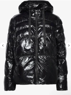 Svart glansig pufferjacka från Guess - Säljer en supersnygg svart, glansig pufferjacka från Guess med huva och dragkedja framtill. Jackan har snörning med Guess-logga på banden. Perfekt för kalla dagar:)
