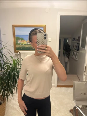 Beige stickad topp med kort ärm - Säljer en stilren beige stickad topp med korta ärmar och rund hals. Toppen har en mjuk och enkel design som passar perfekt till jeans eller kjol. Materialet känns skönt mot huden och ger en avslappnad men ändå snygg look. Storlek xs