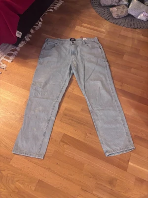 Ljusblå aciid jeansbyxor från Dickies - Säljer ett par ljusblå jeansbyxor från Dickies med raka ben och klassisk femficksdesign. Byxorna har extra fickor på sidan och bak, samt hällor för bälte. Perfekta för dig som gillar en avslappnad och enkel stil.