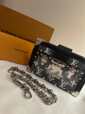 Axelväska med kedja - Säljer en ikonisk svart axelväska med silverfärgade metalldetaljer och kedja. Helt ny