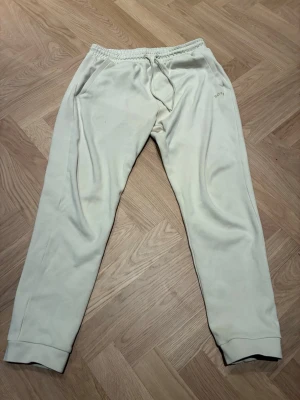 Beiga mjukisbyxor från BOSS - Säljer ett par beiga mjukisbyxor från BOSS med broderad logga vid fickan. Gjorda i mjukt bomullsmaterial. Perfekta för chill dagar eller när du vill vara extra bekväm. Bra skick, en liten lös tråd på vänster lår men det syns ej. Garanterar autenticitet. Storlek S