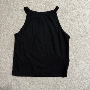 Svart ribbad linnetopp Gina Tricot - Säljer en svart ribbad linnetopp från Gina Tricot i storlek XS. Toppen har hög halsringning och smala axelband, vilket ger en clean och modern look. Materialet är mjukt och stretchigt, perfekt för sommardagar eller att styla lager på lager.