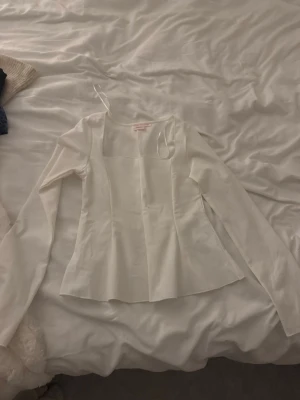 Vit långärmad topp från Gina Tricot - Snygg vit långärmad topp från Gina Tricot med fyrkantig ringning och figurnära passform. Perfekt att styla med jeans eller kjol för en clean look. Materialet känns mjukt och har en lätt glans. OBS!! Den sitter som en S!!