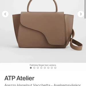 ATP väska  - Stilren beige axelväska i skinn med cool asymmetrisk lockdesign och både handtag och avtagbar axelrem. Väskan har guldfärgade metalldetaljer och rymligt huvudfack, perfekt för att bära med sig allt viktigt. Enkel att matcha och ger en clean look. Använd men bra skick 