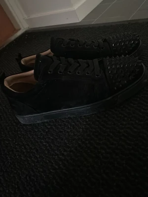 Svarta loubs med nitar - Svarta sneakers i mocka med coola nitar på tån och snörning framtill. Skorna har en låg profil och rund tå, vilket ger en edgy och trendig look. Perfekta för dig som vill sticka ut med detaljer och gillar streetstyle.