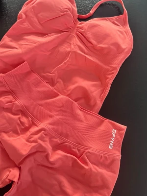 Korallfärgat träningsset från DFYNE - Säljer ett snyggt korallfärgat träningsset från DFYNE med sport-bh och matchande shorts. Setet är sömlöst och har bred resår i midjan för extra komfort. Materialet är stretchigt och passar perfekt till gymmet eller annan träning.