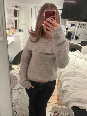 Ljusgrå off shoulder stickad tröja - Mysig ljusgrå stickad tröja med bred off shoulder-krage och långa ärmar. Tröjan har en avslappnad passform och ribbstickade detaljer vid kragen och ärmsluten. Perfekt för lager-på-lager och chill dagar.