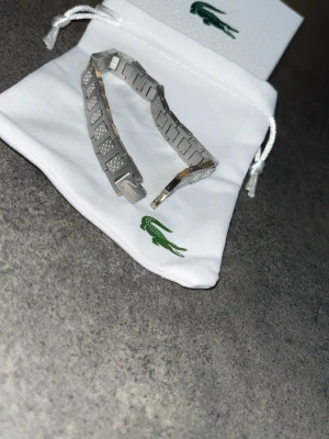 Lacoste armband  - En fin Lacoste armband i ny skick. Allt på bilden ingår. Fraktas snabbt. Pris går att diskuteras vid snabb affär.
