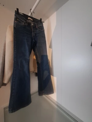 Blå bootcut jeans  - Ett par klassiska blå jeans med bootcut-modell. Jeansen har fem fickor, dragkedja och knapp framtill. Tillverkade i jeansmaterial med en något mörkare tvätt och lätt slitning.
