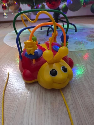 Färgglad larv leksak med tråd - Säljer en färgglad larvformad leksak i plast med stora svarta ögon och ett glatt ansikte. Leksaken har flera böjda metalltrådar med pärlor och figurer att flytta runt samt ett snöre för att dra den efter sig. Perfekt för att träna motorik och koordination.