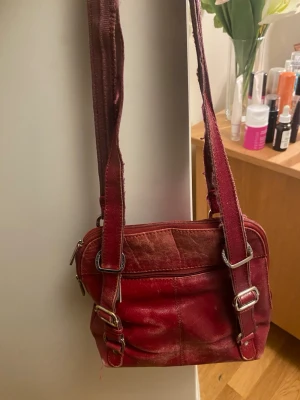Röd axelväska med spännen - Cool röd axelväska i skinn med justerbara axelband och snygga metallspännen framtill. Lite slitage, speciellt på banden.💋