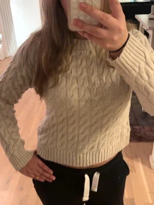 Beige kabelstickad tröja - Säljer en beige kabelstickad tröja med rund hals och långa ärmar. Tröjan har ribbade muddar vid ärmslut och nederkant, och är perfekt för dig som gillar en mysig men ändå trendig look.🤞