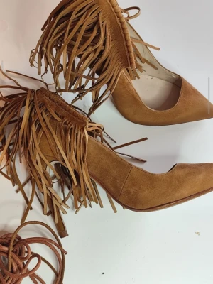 Bruna mocka-pumps med fransar Zara - Snygga bruna pumps från Zara i mocka med spetsig tå och hög klack. Skorna har dekorativa fransar runt ankeln som ger en unik och trendig look. Perfekta för dig som vill sticka ut med dina skor. Du är varmt välkommen att kika på mina andra annonser.