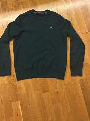 Mörkgrön stickad tröja från Morris - Mörkgrön stickad tröja från Morris i 100% merinoull. Tröjan har rund halsringning, ribbade muddar och en liten broderad logga på bröstet. Perfekt för dig som gillar klassisk och stilren design. Är M men är exakt lika stor som en xs då den har krypt i tvätten, där av säljer jag. Är bara använd en gång. 