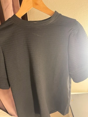 Svart ribbad topp med puffärm - Säljer en svart ribbad topp med kort puffärm. Toppen har en rund halsringning. Smink fläck vid halsringningen, ej testat fläckborttagning 