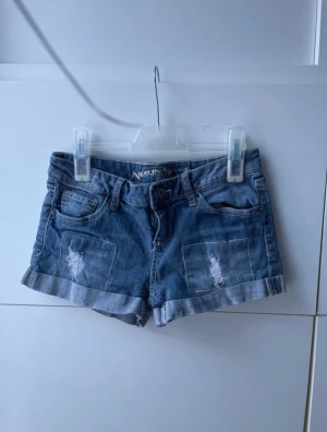 Jeansshorts från Arizona Jean Co - Jeansshorts från Arizona Jean Co – The Original. Storlek 3 (ca XS). Blå denim med fransade detaljer och upprullade ben. Klassisk femficksmodell. Perfekt för vardagsstil, festival eller vintage-look. Fint skick!