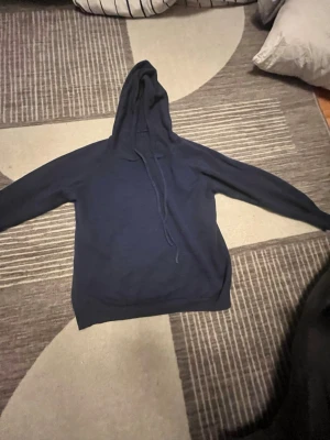 Kasmirhoodie marinblå - En enkel och stilren mörkblå hoodie med luva och dragsko. Tröjan har långa ärmar och ribbade muddar vid ärmslut och nederkant. Perfekt för en avslappnad och bekväm stil.