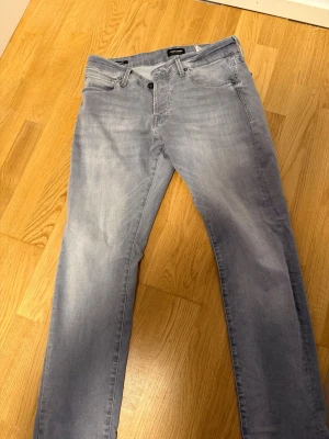 Ljusblå jeans från Jack & Jones - Säljer ett par ljusblå jeans från Jack & Jones med klassisk femficksmodell och knappgylf. Jeansen har en rak passform och är tillverkade i mjukt denimtyg som ger en avslappnad look. Perfekta till vardags för en stilren outfit.