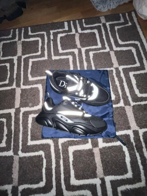 Svarta Dior sneakers med reflexdetaljer - Snygga svarta sneakers från Dior med vita och reflekterande detaljer. Skorna har chunky sula, mesh och skinnpaneler samt snörning. Perfekta för dig som vill sticka ut med en exklusiv look.