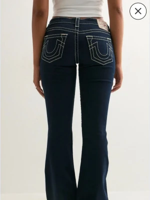 Mörkblå bootcut jeans med kontrastsömmar - Helt nya True Religion jeans i modellen ultra low rise flare big T. Tyvärr fel storlek för mig. Nypris 1399, slutsålda! Kom med prisförslag! SÄLJER ÄVEN ETT PAR I STORLEK 26