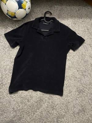 Svart polotopp från Lexington - Klassisk svart polotopp från Lexington i mjukt material. Frotté har korta ärmar och krage med öppen halsringning, perfekt för en clean och stilren look.