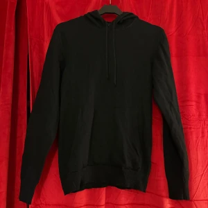 J.Lindeberg Svart Marinull Hoodie M - En stilren svart hoodie med huva. Modellen är enkel, perfekt för en avslappnad look och lätt att matcha med andra plagg. Materialet känns mjukt och bekvämt. Det finns ett litet slitage på fickan framtill men inget märkvärdigt.