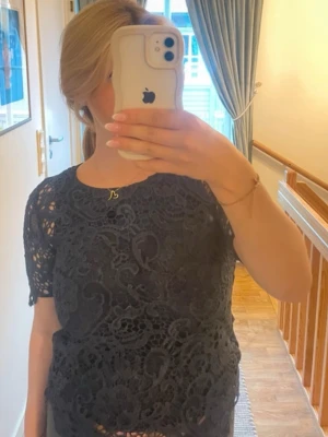 Svart spetsblus med kort ärm - Snygg svart blus i spets med korta ärmar och rund hals. Blusen har ett detaljerat spetsmönster som ger en elegant och trendig look. Från Stockh  LM i storlek 36