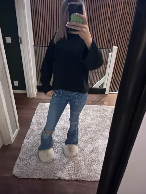 Blå bootcut jeans med slitningar - Säljer ett par blå bootcut jeans med slitningar på knäna. Jeansen har en klassisk femficksmodell och är tillverkade i denim med en snygg tvätt. Perfekta för dig som gillar en avslappnad men trendig stil.
