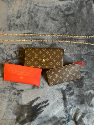 Louis Vuitton Monogram handväska - Säljer en klassisk Louis Vuitton handväska i brunt monogrammönster med guldfärgad kedja. Väskan kommer med en matchande monogram clutch och ett rött kortfodral. Perfekt för dig som gillar lyxiga detaljer och ikonisk design.