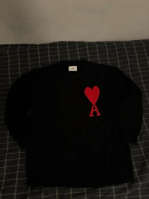 Svart stickad tröja från Ami Paris - Säljer en svart stickad tröja från Ami Paris med deras ikoniska röda hjärta och A på bröstet. Tröjan har rund halsringning, långa ärmar och ribbade muddar. Perfekt för dig som vill ha en clean men ändå statement look. Bara testad på annars nyskick, inga defekter. Hör av dig om du har några frågor.:) Kan gå ner till 500 vid snabb affär behöver få såldt snabbt