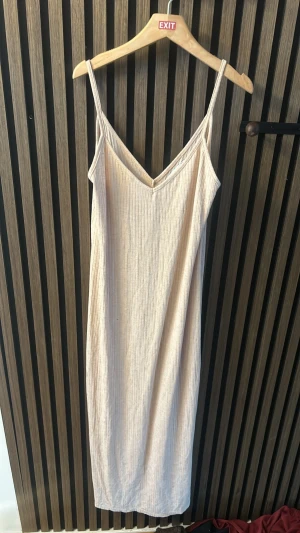 Beige ribbad klänning Bershka - Säljer en beige ribbad klänning från Bershka i storlek S. Klänningen har smala axelband, v-ringning och är i ett mjukt, stretchigt material. Perfekt för sommardagar eller att styla med en tröja över. Enkel och stilren design som är lätt att matcha.