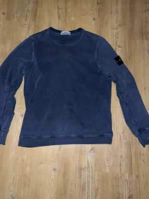 Blå sweatshirt från Stone Island äkta - Säljer en blå sweatshirt från Stone Island med klassisk rund hals och lång ärm. Tröjan har den ikoniska Stone Island-loggan på vänster ärm och är tillverkad i mjukt bomullsmaterial. Perfekt för en avslappnad och stilren look. Självklart äkta nypris 3000