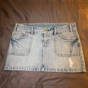 Ljusblå jeanskjol från American Eagle - Snygg ljusblå jeanskjol från American Eagle med klassisk femficksdesign, bälteshällor och slitna detaljer framtill. Kjolen är kort och har en rak passform, perfekt till sneakers eller boots. Tidlös denimstil som alltid funkar. Mått: 43cm 